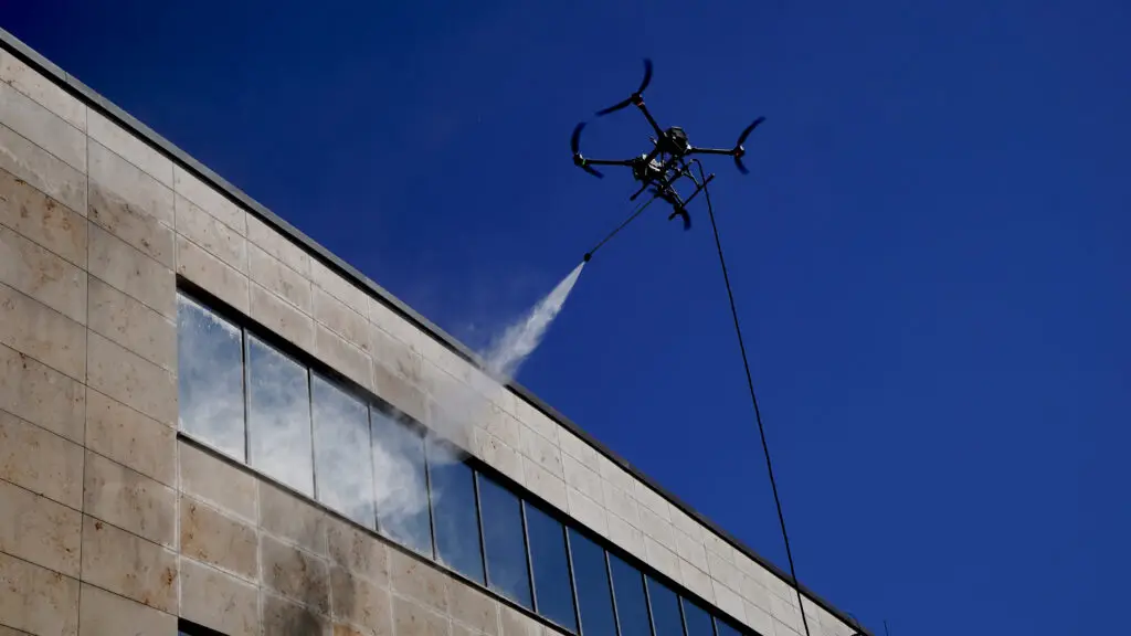 Drooniga fassaadipesu kõrghoonel, veevoolikusüsteemiga, survepesudroon tööhoos